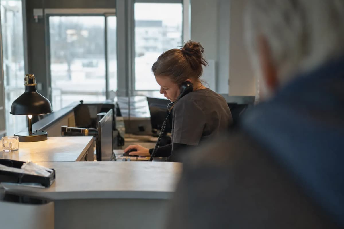 Receptionist ved skranken i en tandklinik med tidsbogen åben på skærmen