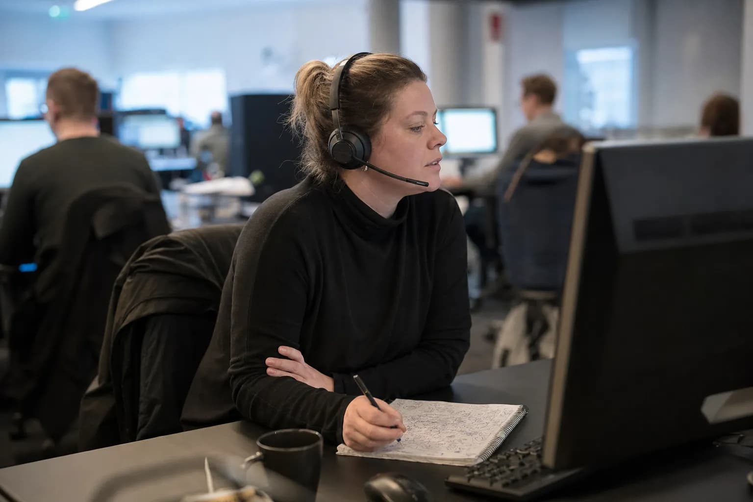 En kundebehandler med hodetelefoner ved pulten i et åpent kontorlandskap