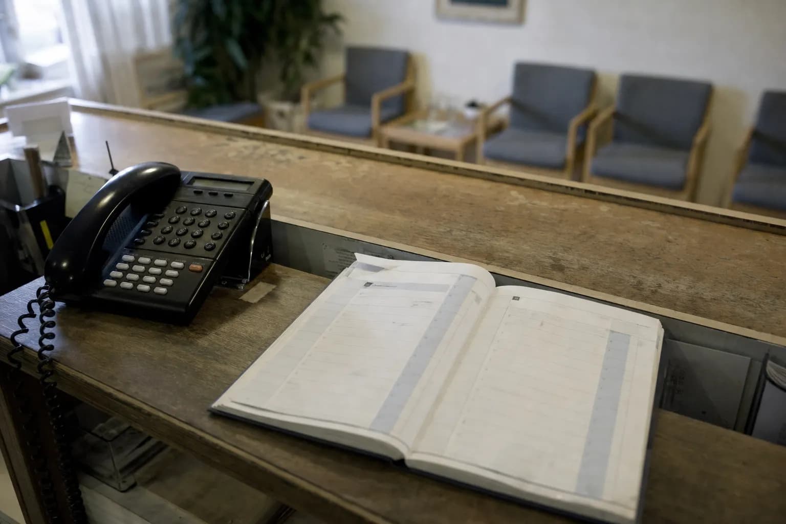 Resepsjonen på et legekontor med avtalebok og telefon, venterommet tomt bak