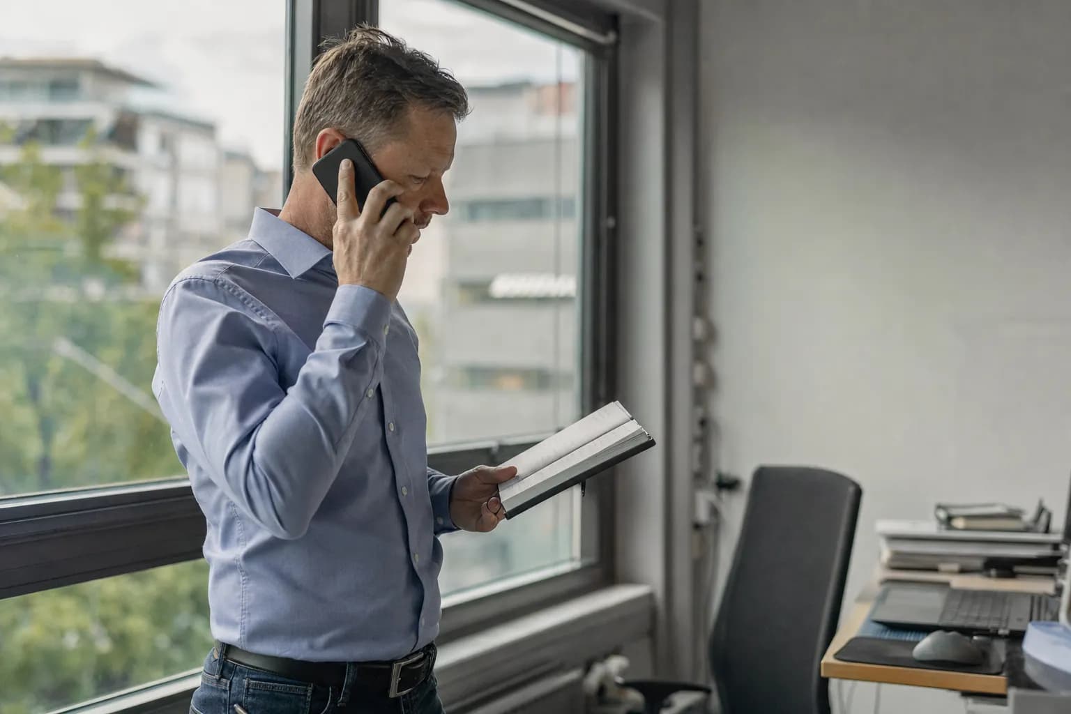 En selger ved vinduet med mobilen mot øret og en notatbok i hånda