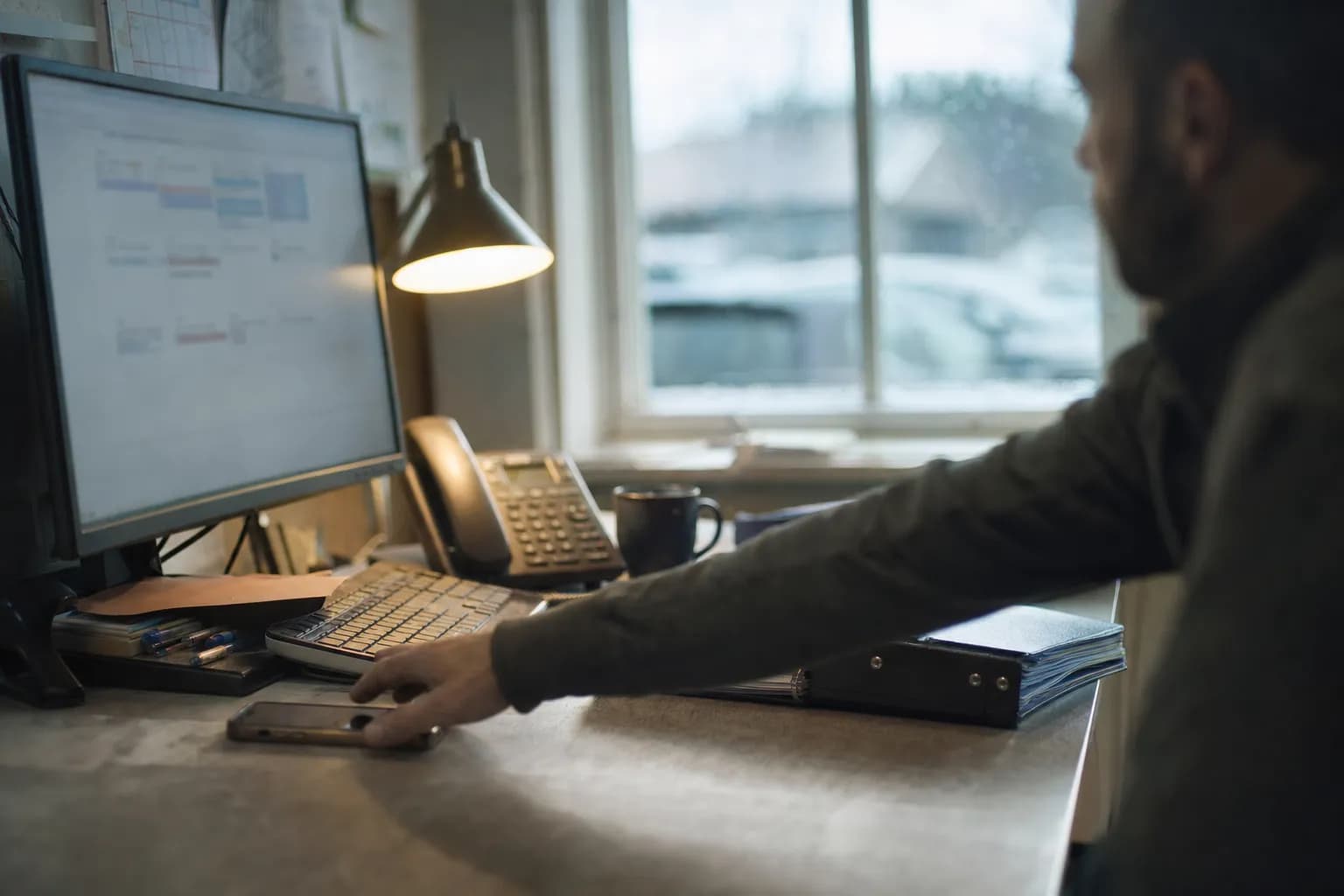 A screen with the calendar open in a small office, the phone lying in front of the keyboard
