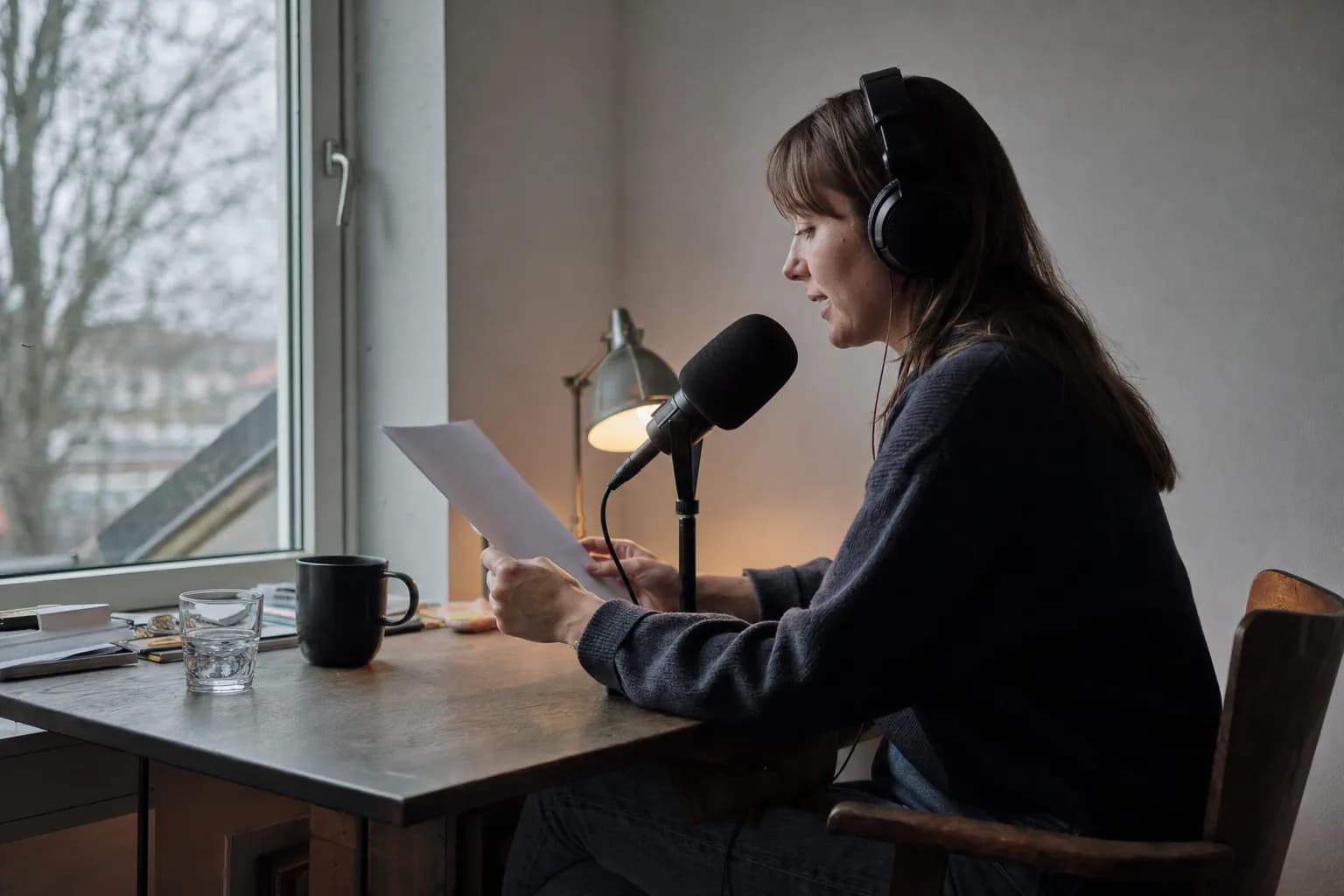 A participant in headphones reading into a microphone at a plain table in an ordinary room