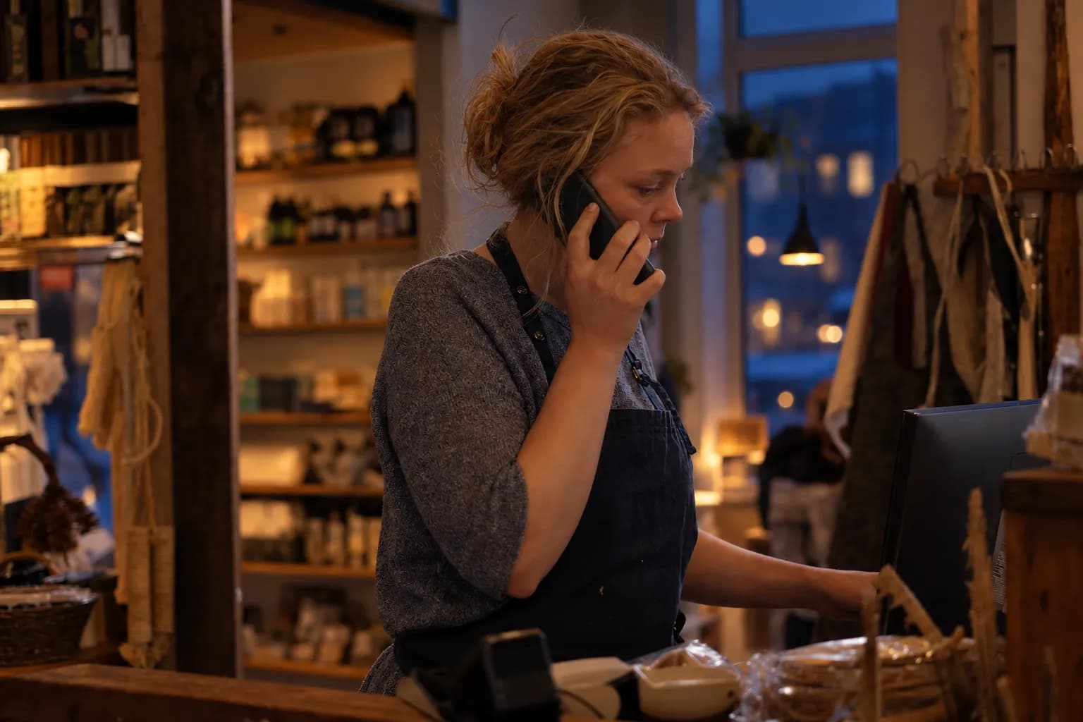 En butikkeier bak disken i en liten butikk med mobilen mot øret