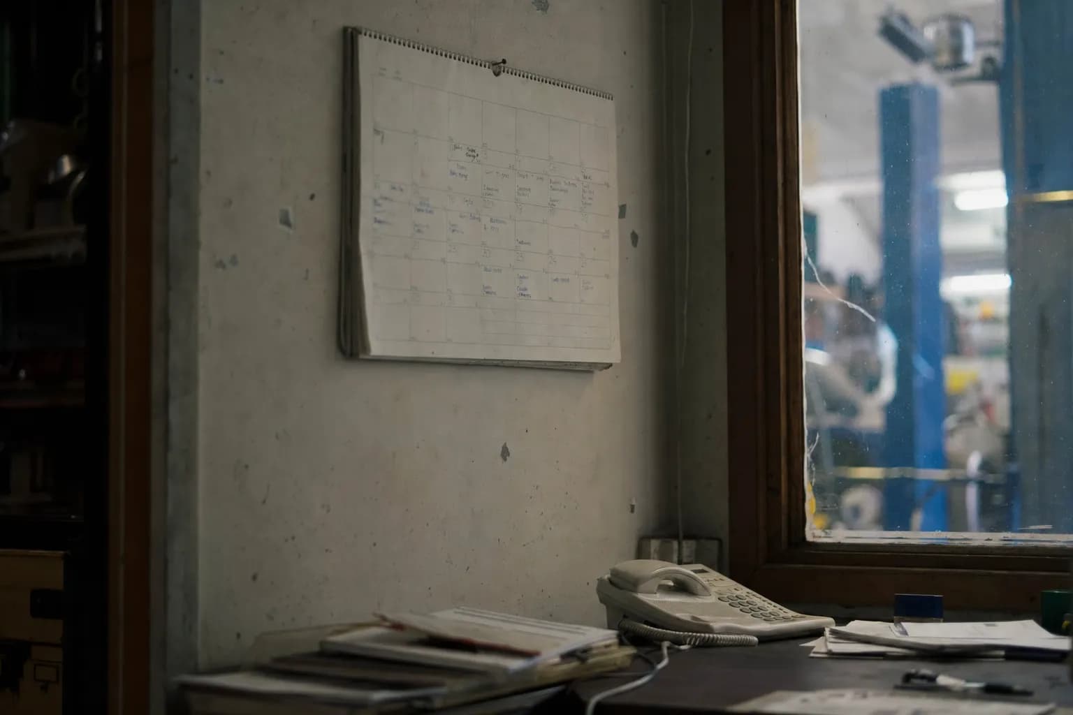 A wall calendar of handwritten appointments above a desk with a phone on it