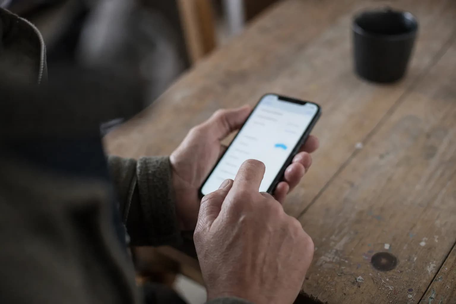 A hand filling in a form on a phone above a worn wooden table